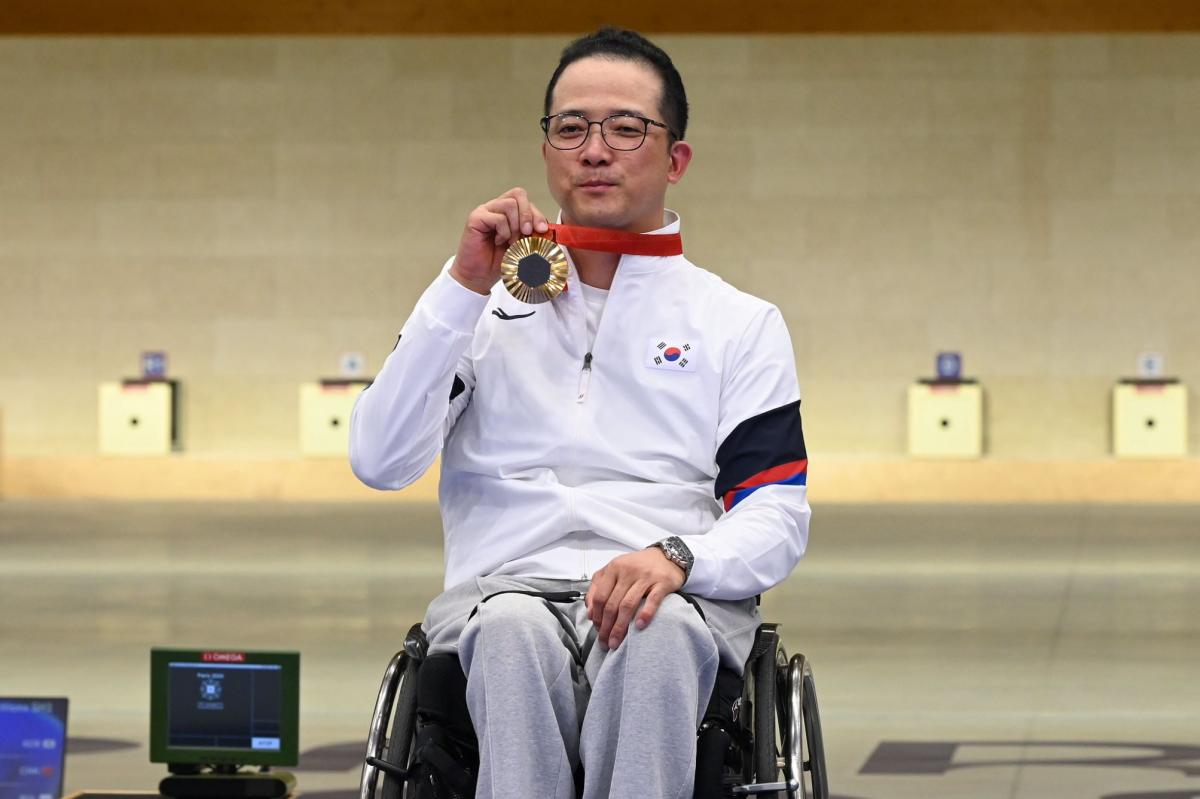 A man in a wheelchair showing his gold medal in a shooting range